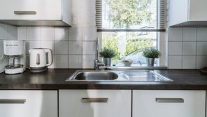 Eine moderne Küche mit weißen Schränken, einer Edelstahlspüle, einer Kaffeemaschine und einem Fenster mit Jalousien.