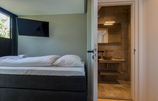 Un dormitorio con cama, televisor de pantalla plana en la pared y baño con lavabo y espejo.