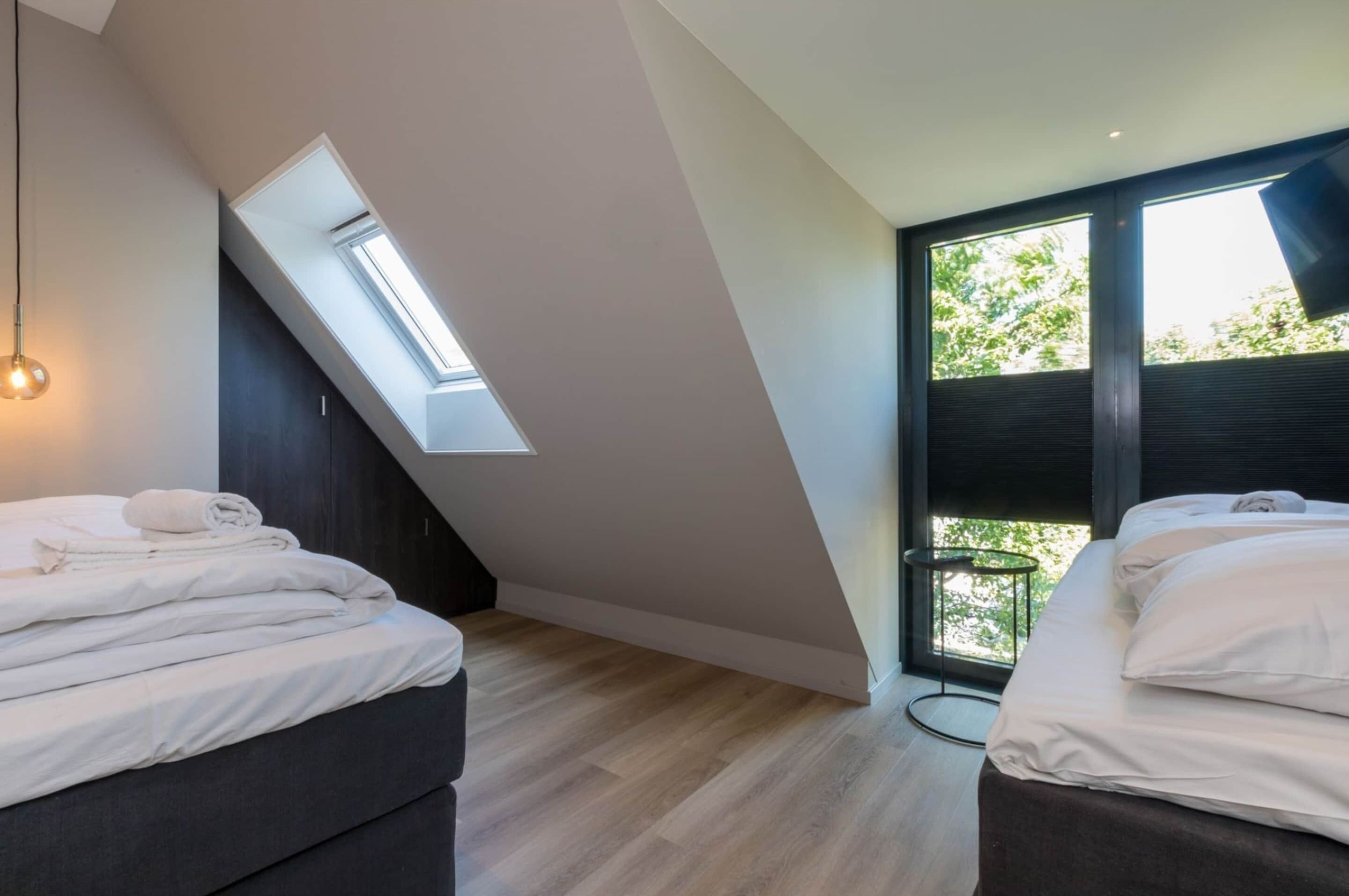 Ein modernes Schlafzimmer mit Dachfenster, zwei Betten und einem großen Fenster.