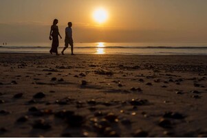 Escena de playa con dos personas caminando hacia el atardecer.