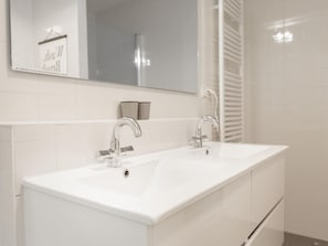 Une salle de bain moderne avec deux lavabos, un grand miroir et un porte-serviettes.
