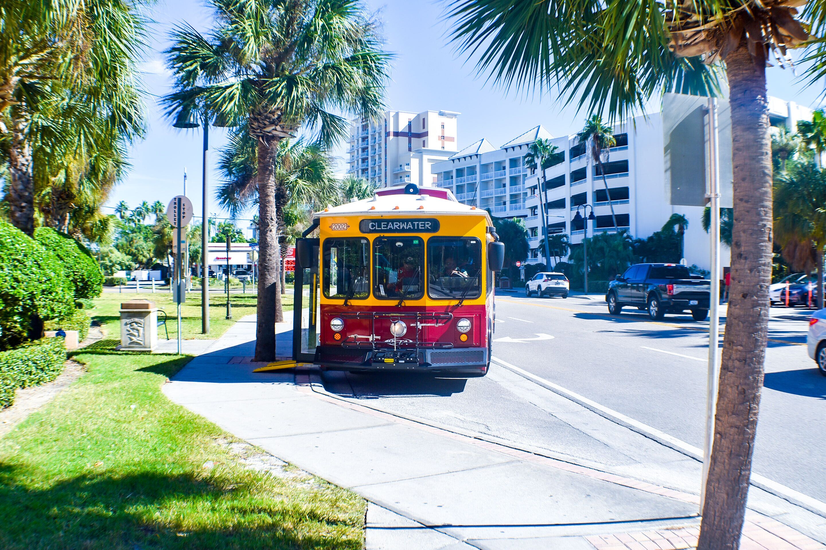 Un tramway jaune et rouge portant l’inscription « CLEVELAND » circule dans une rue bordée de palmiers, avec des bâtiments en arrière-plan.