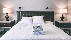 Un lit bien fait, avec du linge de lit blanc et des oreillers, une serviette pliée posée sur le lit, et deux lampes de chevet sur les tables de nuit.
