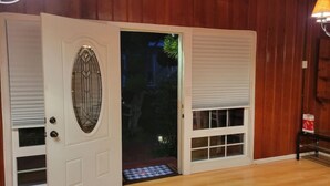 Un intérieur en bois avec une porte blanche ornée d’un panneau de verre décoratif et un petit seuil menant à l’extérieur.