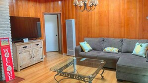 Un salon chaleureux avec un mur en bois, un canapé gris, une table basse en verre et un meuble en bois.