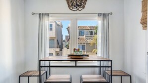 A dining area with a table and chairs, a view of buildings outside, and a window with curtains. - MB Gem Lower - Steps To The Beach, Ocean Breeze (Manhattan Beach)