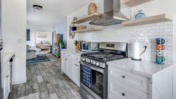 A modern kitchen with white cabinets, a stainless steel stove, and wooden shelves. - MB Gem Lower - Steps To The Beach, Ocean Breeze (Manhattan Beach)