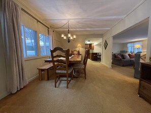 A dining area with a wooden table and chairs, a chandelier, and a view of the kitchen and living room through an open doorway. - Spacious Marquette Getaway  Trails Nearby  Perfect 4-Season Basecamp (Marquette)