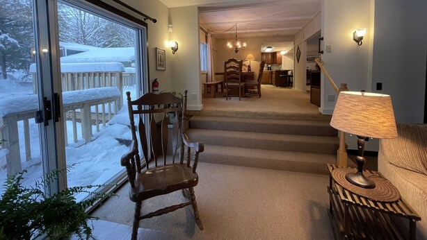 A cozy interior with a wooden chair, a lamp, and a view of a snowy deck through a glass door. - Spacious Marquette Getaway  Trails Nearby  Perfect 4-Season Basecamp (Marquette)