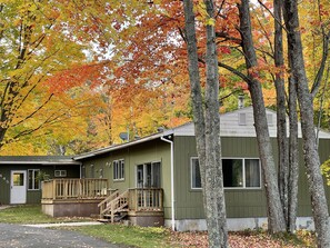 A two-story building with a green exterior, a wooden deck, and a visible staircase leading to the upper level. - Spacious Marquette Getaway  Trails Nearby  Perfect 4-Season Basecamp (Marquette)