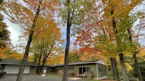 A single-story building with a green exterior, a front porch, and a driveway leading to a garage. - Spacious Marquette Getaway  Trails Nearby  Perfect 4-Season Basecamp (Marquette)