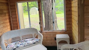 A wooden cabin interior with wicker furniture, large windows, and a view of a green landscape. - Spacious Marquette Getaway  Trails Nearby  Perfect 4-Season Basecamp (Marquette)