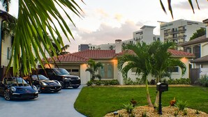 A residential area with a house featuring a red-tiled roof, a driveway with parked cars, and a well-maintained lawn with palm trees. - Devon Shores - Waterfront House (Clearwater)