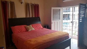 A bedroom with a bed, curtains, a nightstand, and a window with blinds. - Flagstaff Home Away From Home (Port of Spain)