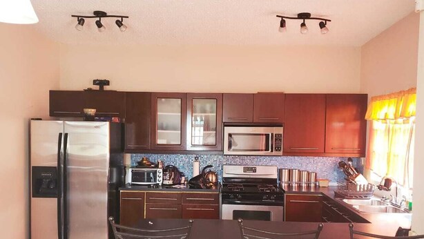A modern kitchen with stainless steel appliances, dark wooden cabinets, and a dining area with metal chairs. - Flagstaff Home Away From Home (Port of Spain)