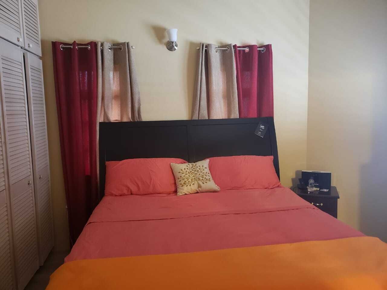 A bed with a black headboard, red and orange bedding, and a decorative pillow.
