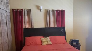 A bed with a black headboard, red and orange bedding, and a decorative pillow. - Flagstaff Home Away From Home (Port of Spain)