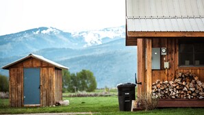 Eine Holzhütte mit einem Metalldach, ein kleines Gartenhaus und ein Berg im Hintergrund.