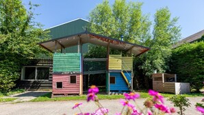Estrutura de madeira em vários níveis com telhado de metal, cercada por vegetação e flores.