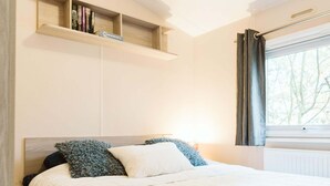 A bedroom with a bed, a bedside table, a shelf with books, and a window with curtains. - Luxury Chalet for Lovers of Peace, Nature (Goedereede)