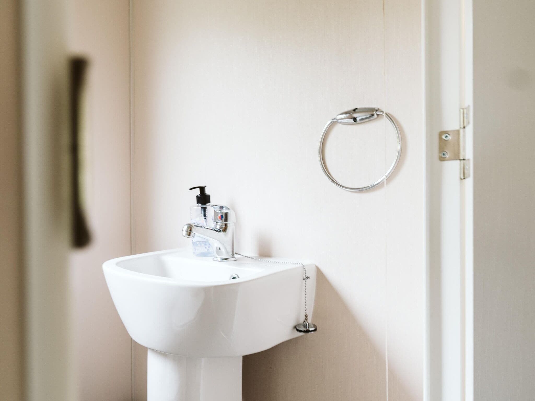 A white bathroom sink with a soap dispenser and a towel ring on the wall.