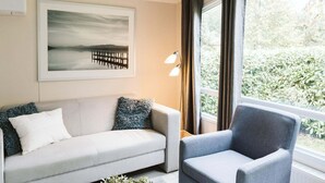 A room with a sofa, a chair, a lamp, a painting, and a window with curtains. - Luxury Chalet for Lovers of Peace, Nature (Goedereede)