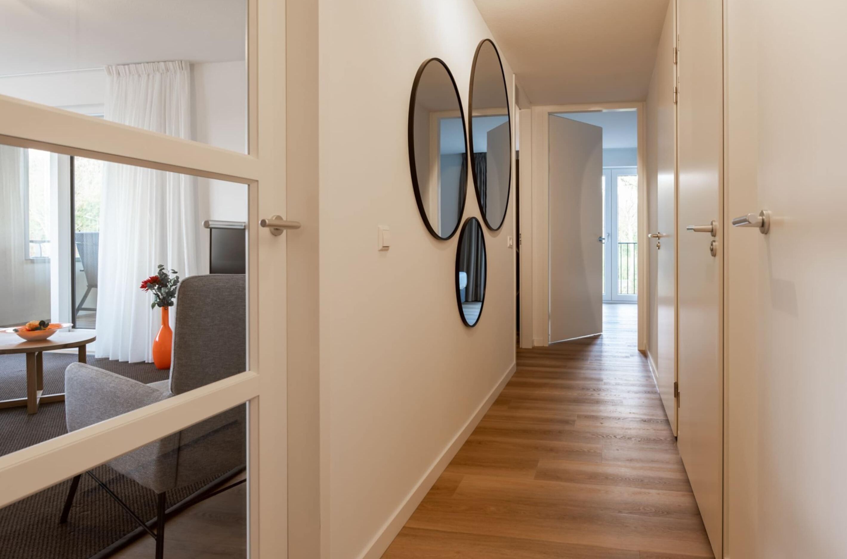 A hallway with a wooden floor, a dining area with a table and chairs, and a large window with curtains.