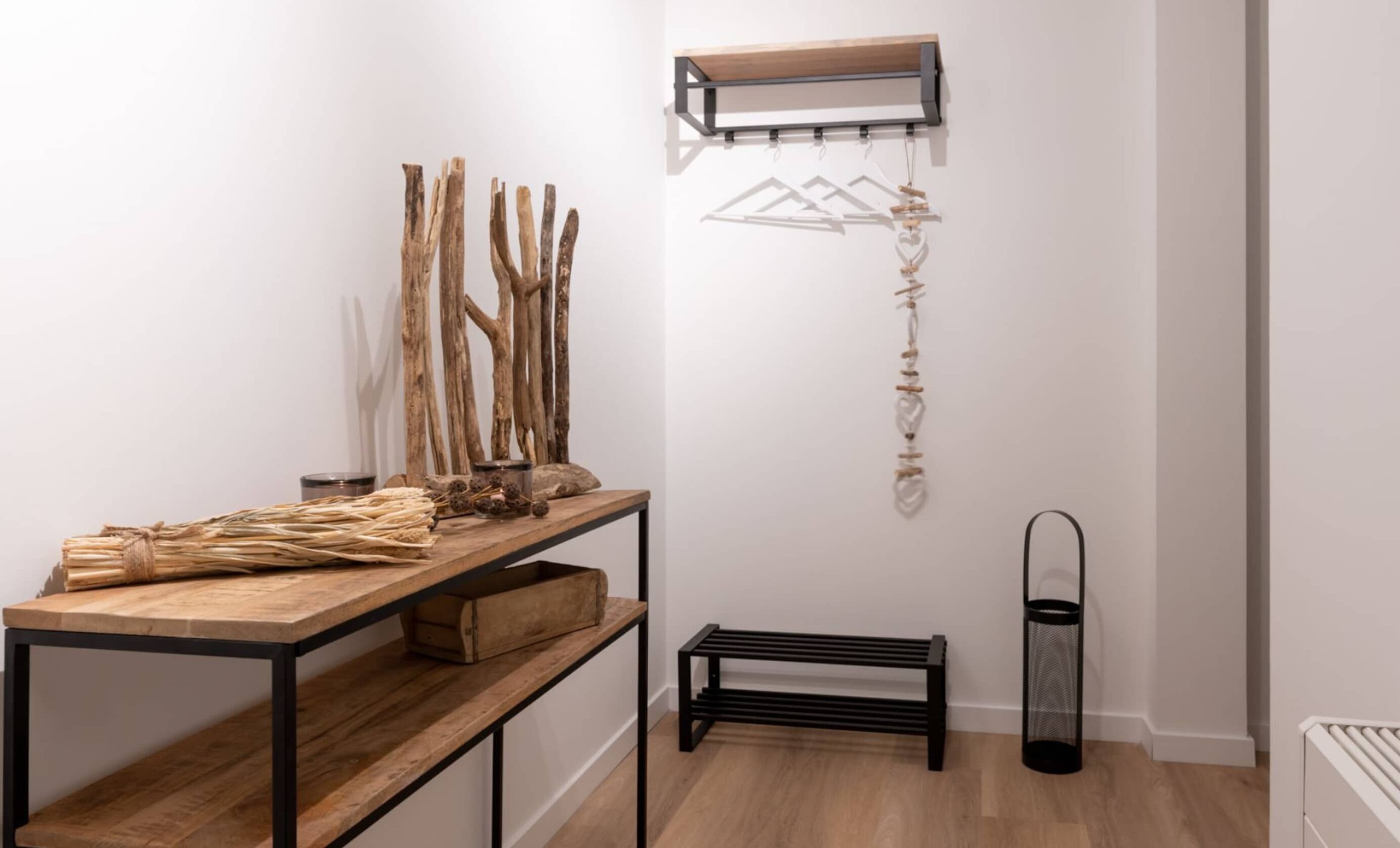 Une pièce au décor minimaliste, avec une table en bois, des étagères, un luminaire suspendu et un radiateur.