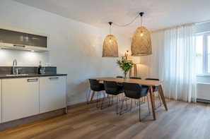 Uma cozinha moderna com forno embutido, uma área de refeições com mesa de madeira e cadeiras pretas, e uma grande janela com cortinas brancas.