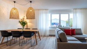 A modern living room with a sofa, dining table with chairs, and two hanging lights. - Luxury Apartment in Kamperland (Kamperland)