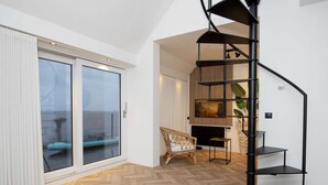 Un intérieur moderne avec un escalier en colimaçon, une grande porte-fenêtre coulissante et un parquet en bois disposé en point de Hongrie.