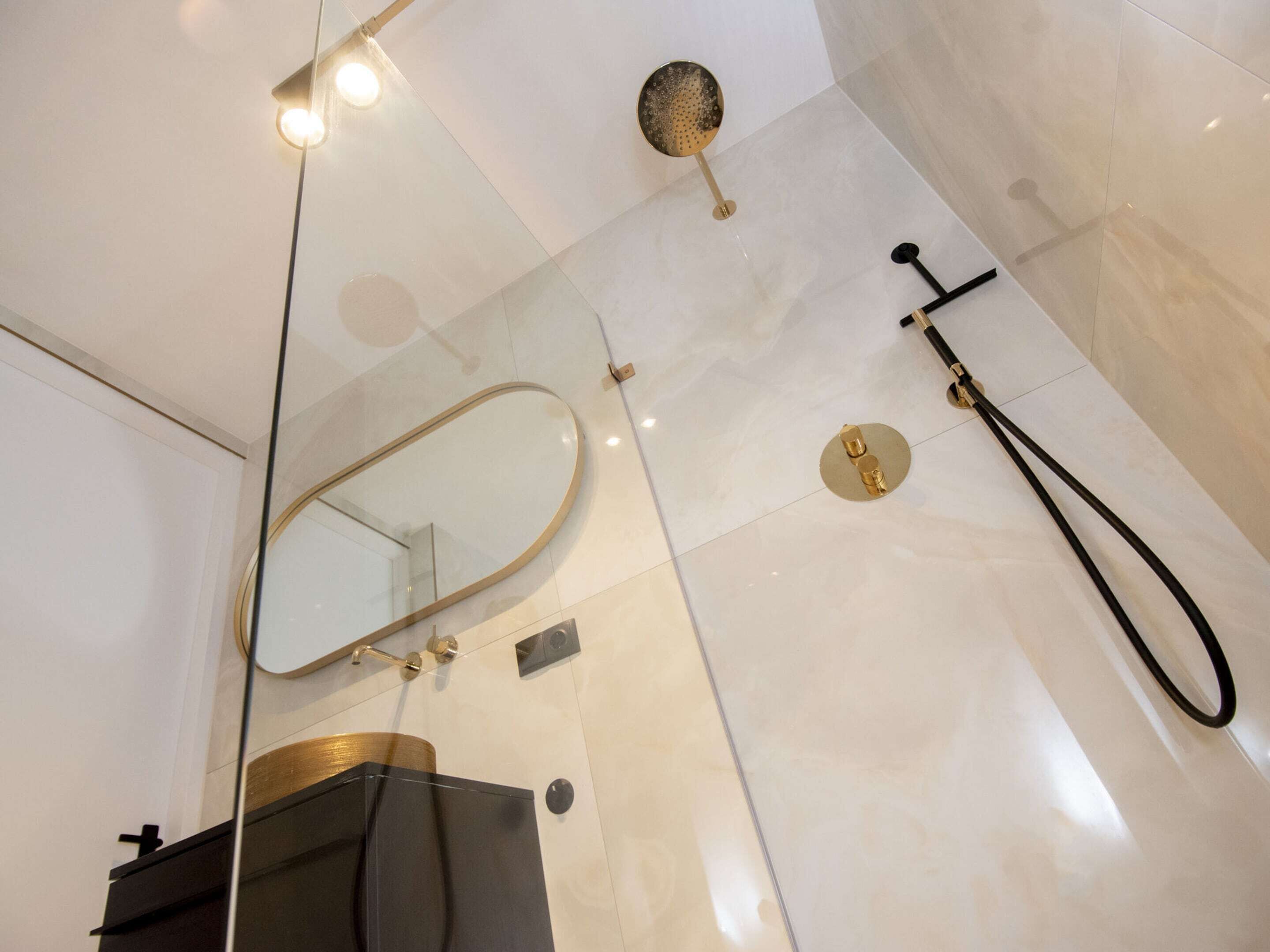 Een moderne badkamer met een douchecabine van glas, een gouden douchekop en een grote spiegel.
