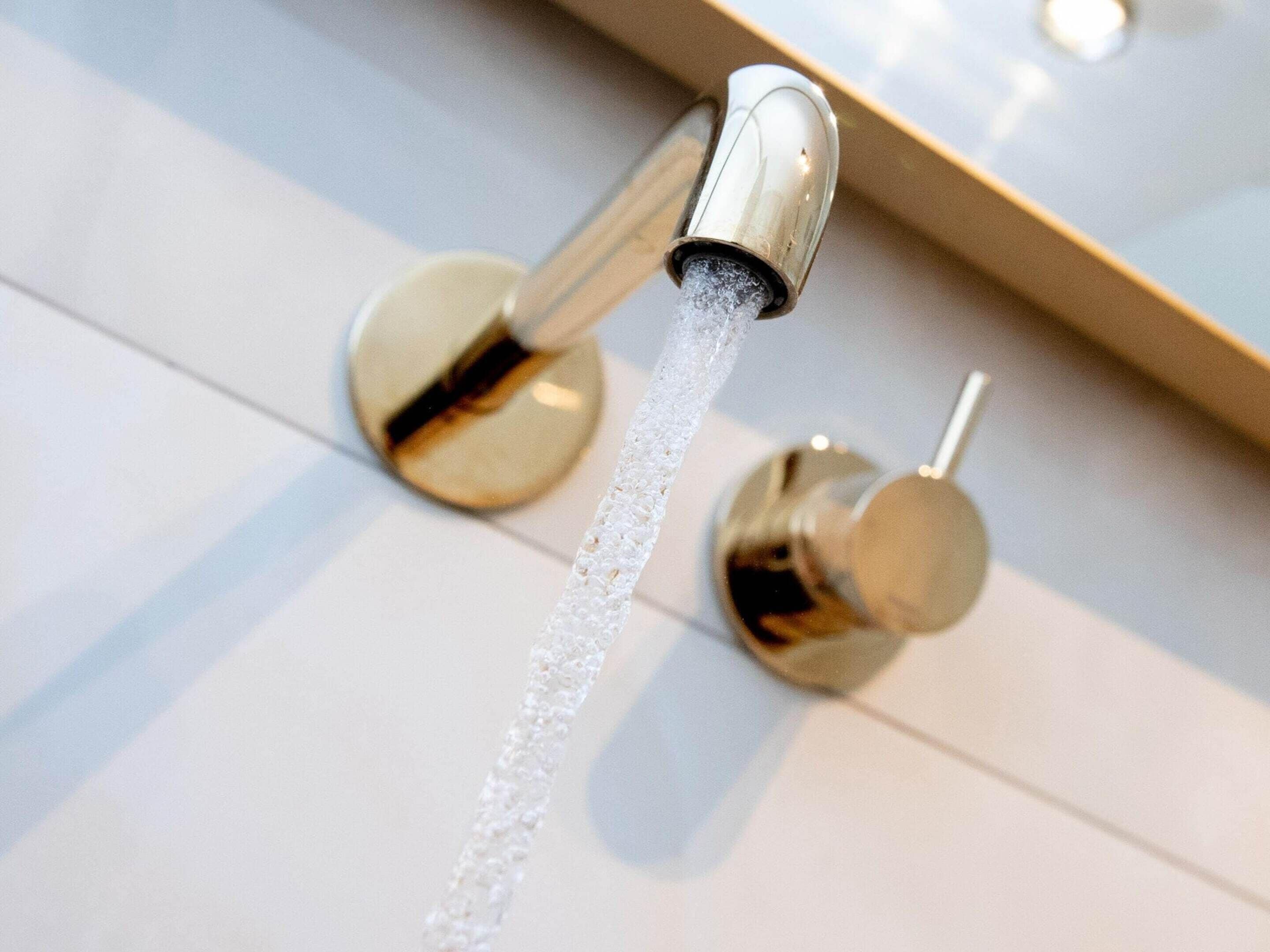 Un bagno moderno con un rubinetto cromato e un getto d'acqua visibile.
