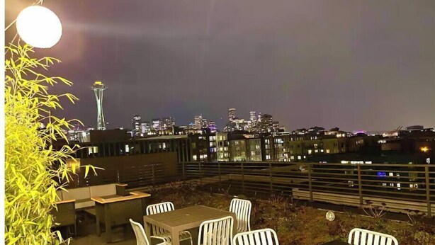 Un espace de restauration en plein air, avec des tables et des chaises, offrant une vue sur les lumières de la ville la nuit.