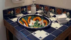 A bathroom with a wooden towel rack, a mirror with floral design, and a sink with a floral tile backsplash.
