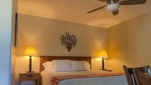A bedroom with a bed, two bedside lamps, a ceiling fan, and a wall-mounted plant.