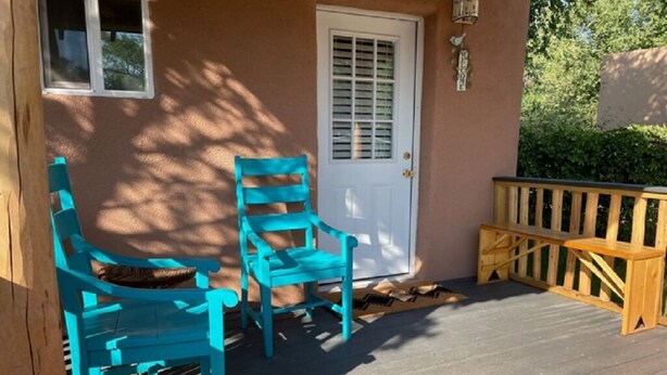 A porch with two turquoise chairs, a wooden bench, and a white door.