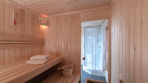 A wooden sauna room with benches, a wooden bucket, and a glass door leading to a shower area. - Villa in Zeeland With Jacuzzi and Sauna (Colijnsplaat)
