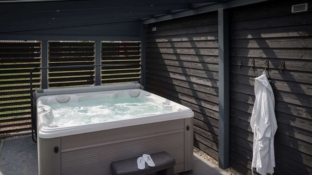 A hot tub with a bench and step, a towel rack, and a wooden wall. - Villa in Zeeland With Jacuzzi and Sauna (Colijnsplaat)