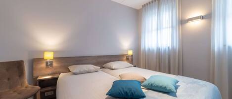 A hotel room with a large bed, two bedside tables with lamps, a chair, and a window with curtains.