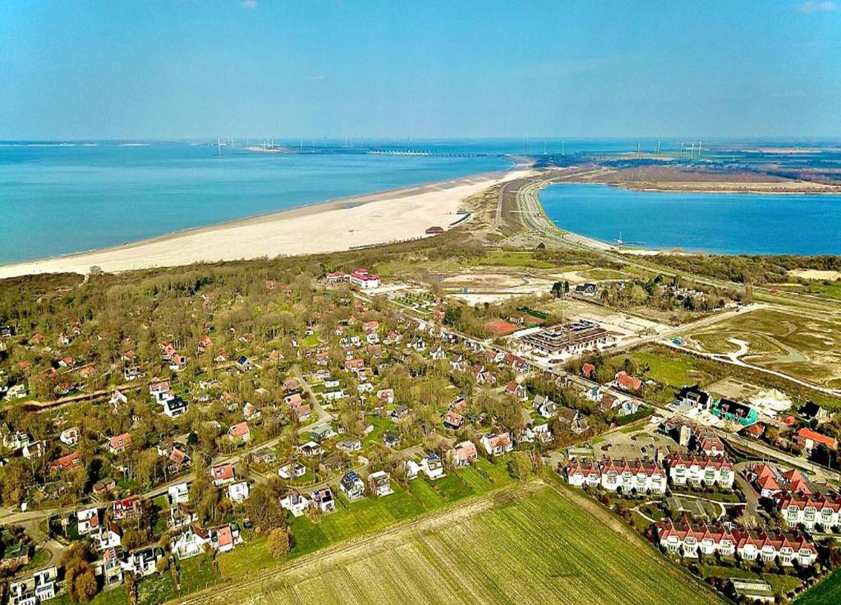 Una vista aerea di una localit à costiera con spiaggia, zone residenziali e un ampio specchio d'acqua.