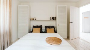 Une chambre à coucher avec un grand lit, deux tables de chevet, une étagère avec des livres et des objets décoratifs, et une armoire dont la porte est ouverte sur le côté droit.
