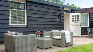 Un espace patio aménagé avec des meubles en osier, une table en verre et un vase rempli de fleurs.