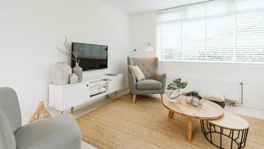 Un salon moderne avec un téléviseur à écran plat, un fauteuil gris, une table basse en bois et un meuble console blanc.