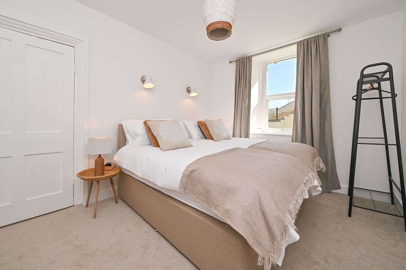 A bedroom with a bed, a bedside table, a lamp, a window with curtains, and a ladder.