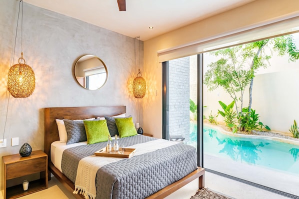 A modern bedroom with a large bed, bedside tables, a round mirror, and a view of an outdoor swimming pool.