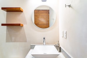 A bathroom with a white sink, wooden shelves, a round mirror, and a wooden door.