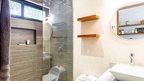 Een moderne badkamer met een douchecabine van glas, een toilet, een wastafel en houten planken boven de spiegel.