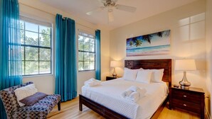 A bedroom with a large bed, two bedside tables, a chair, and a ceiling fan.