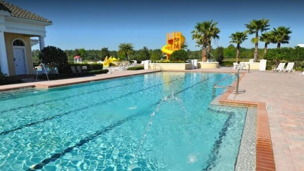 A swimming pool with clear blue water, a diving board, and lounge chairs.
